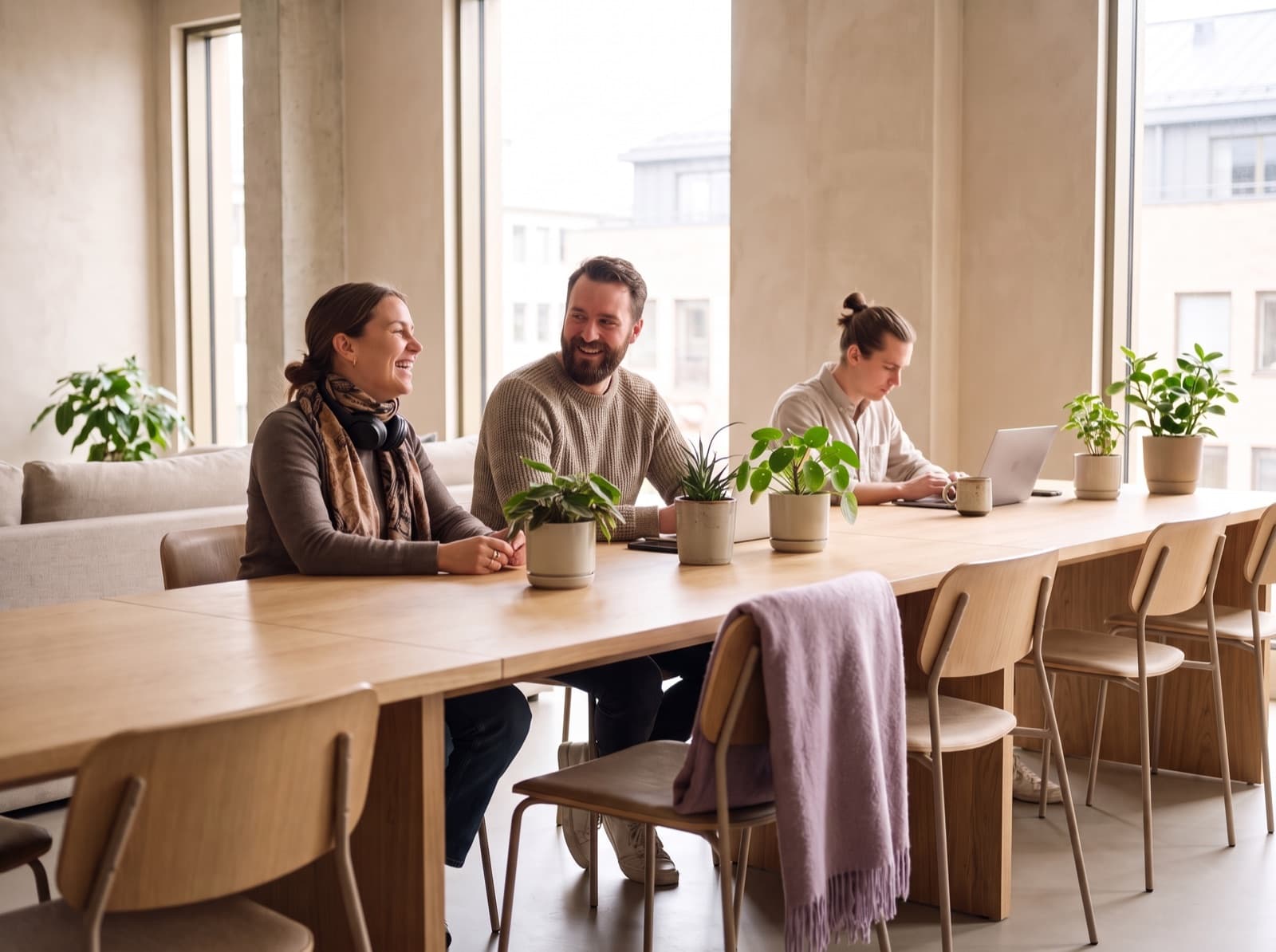 Equipo de soporte de tres personas en una mesa larga de roble, con computadoras portátiles y plantas.